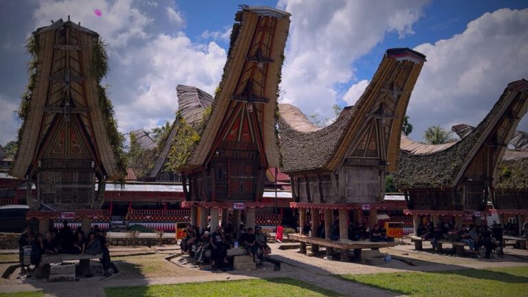 Tradycyjne domy Tongkonan w Tana Toraja na Sulawesi, z ludźmi siedzącymi przed nimi podczas uroczystości.